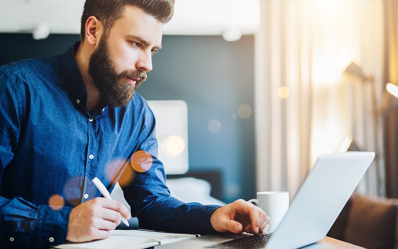 Businessman on laptop computer while taking notes in notebook